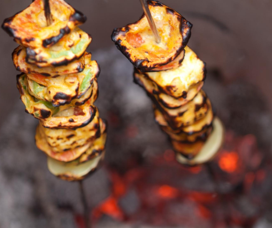 skewered vegetables being lowered into tandoor oven